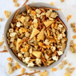 A gray bowl filled with seasoned pretzels, bugels, gold fish, popcorn, peanuts and chex cereal.