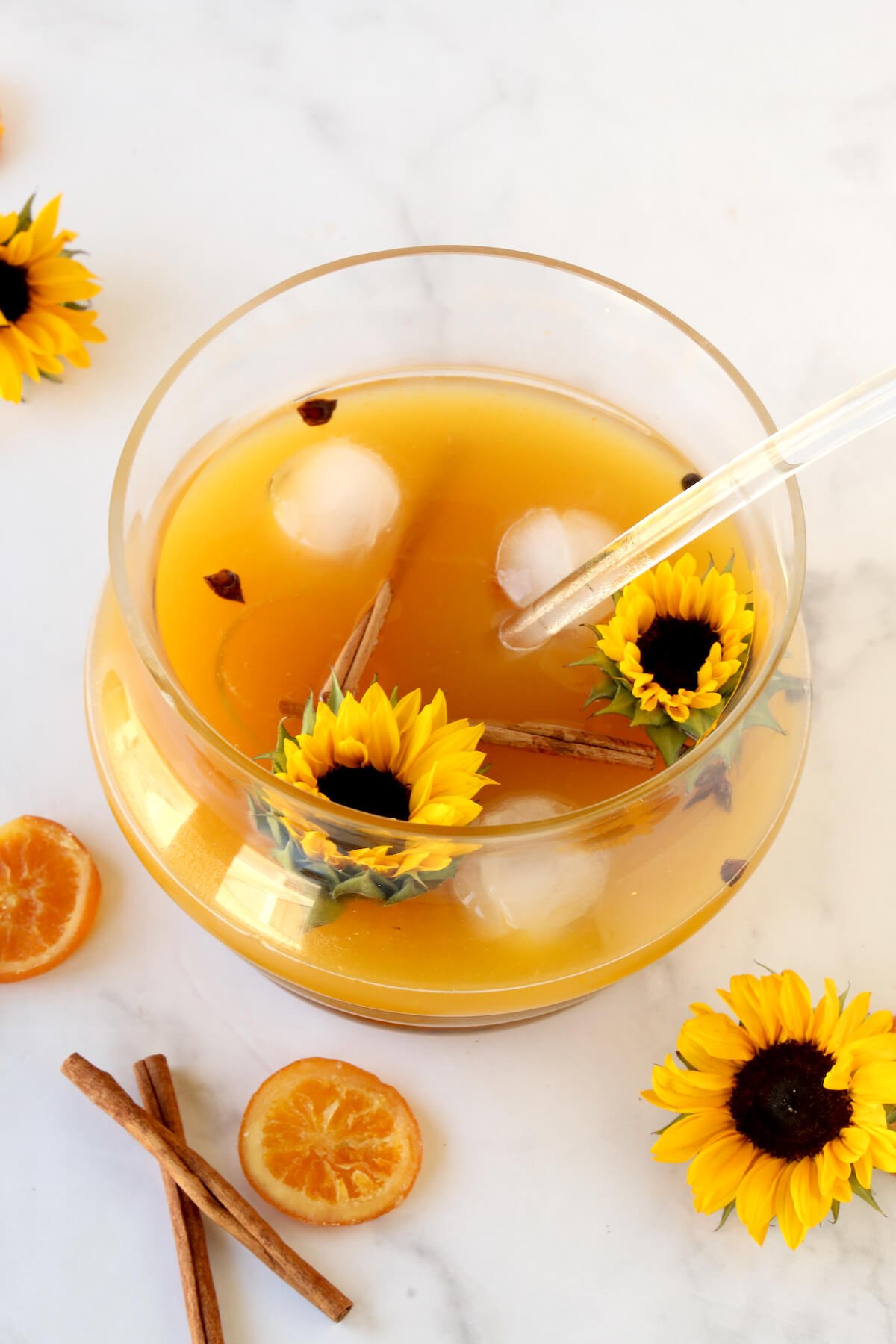 A punch bowl filled with orange cocktail, surrounded by sunflowers. 