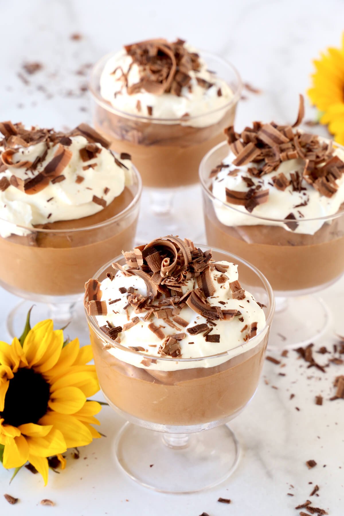 Four clear glass bowls filled with chocolate mousse, whipped cream and chocolate shavings.