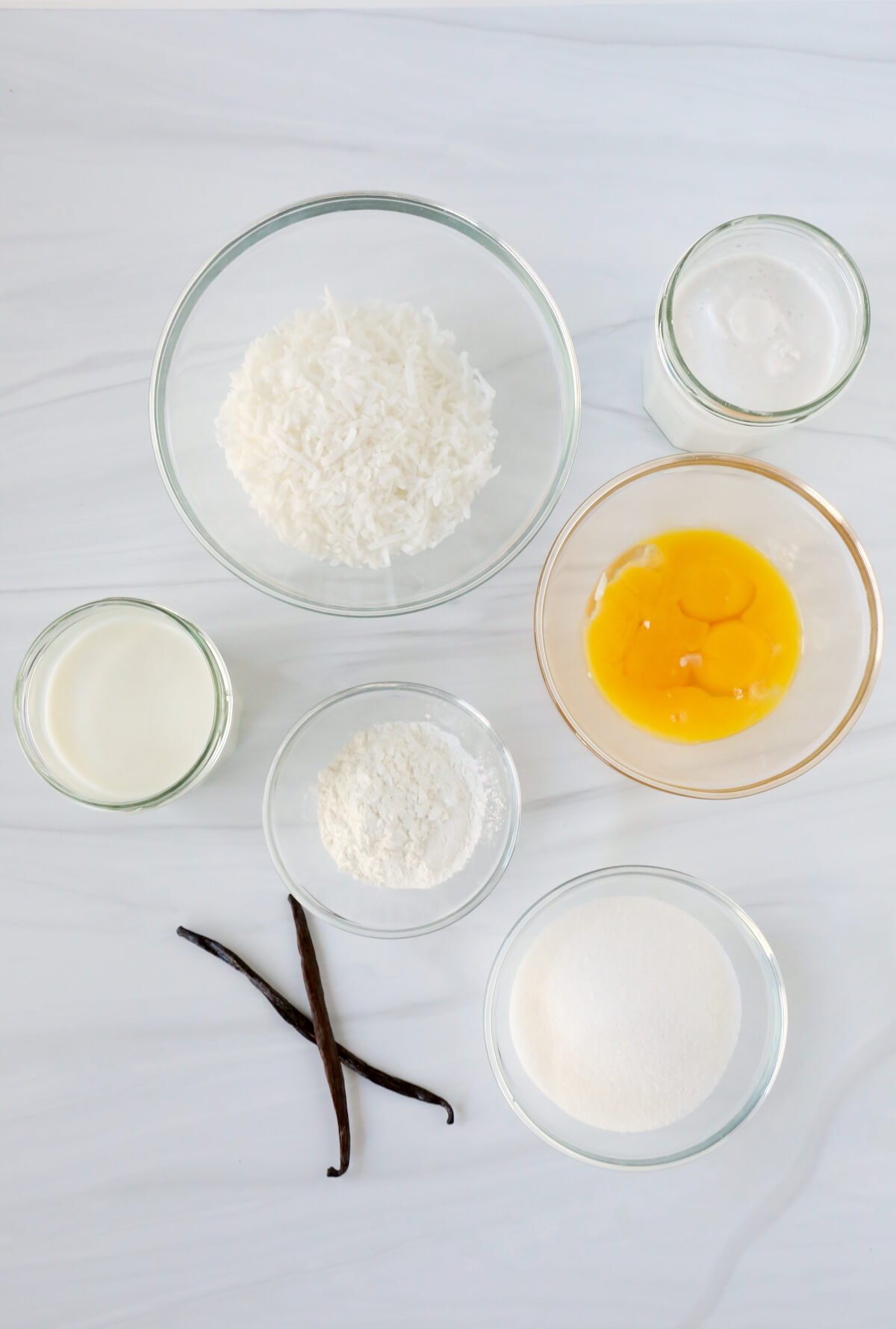 bowls of sugar, egg yolks, cornstarch, milk and coconut milk sitting next to two vanilla bean pods.  