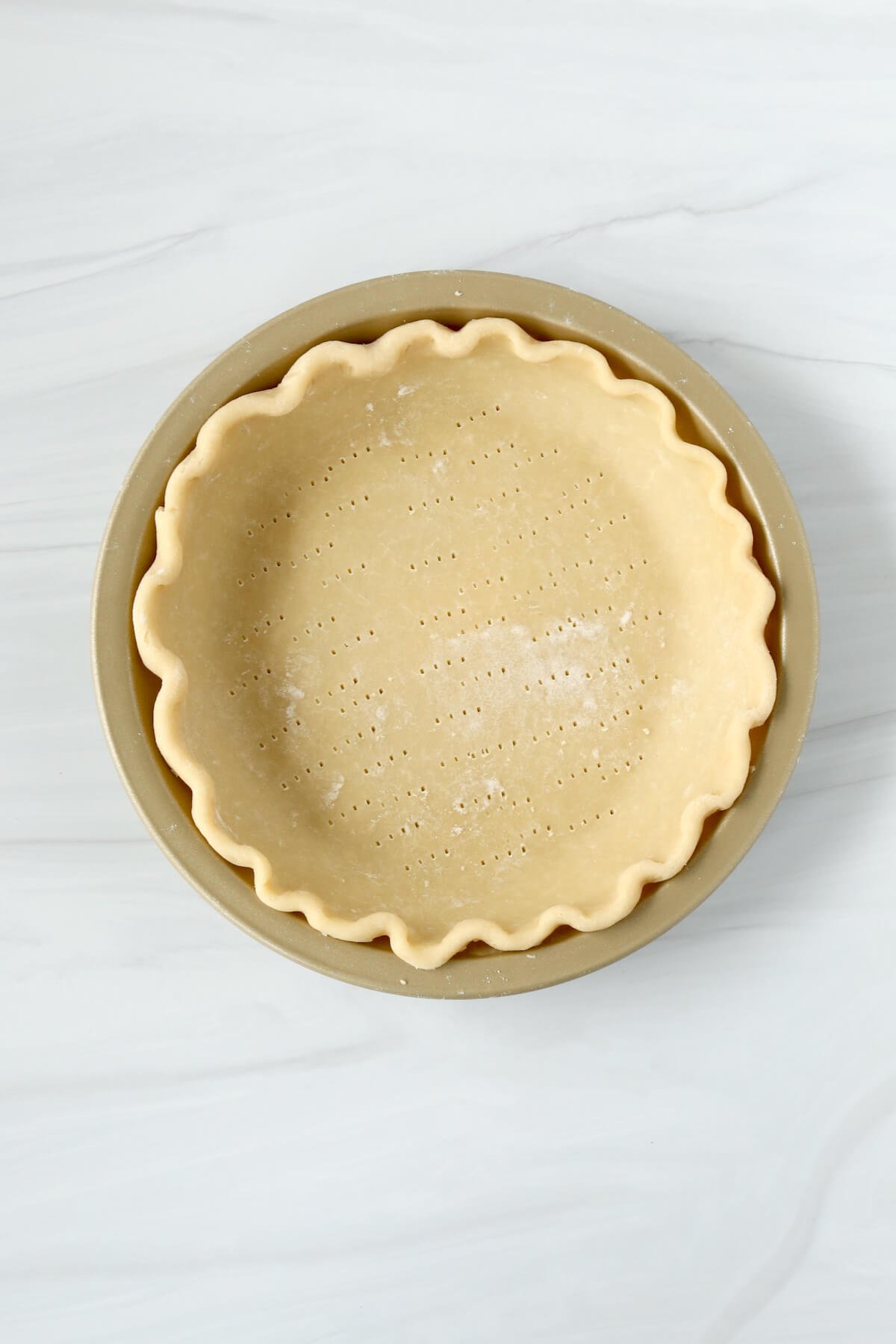 A gold pie plate with pie dough formed into it.  