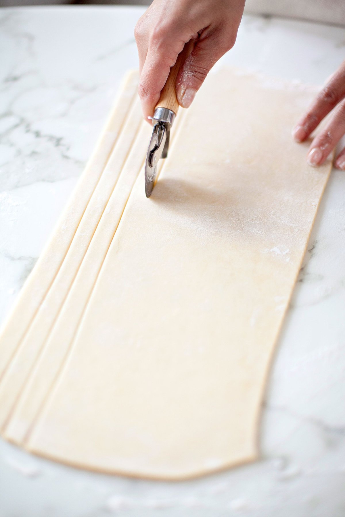 Dough rolled out on a table being cut with a pastry cutter. 