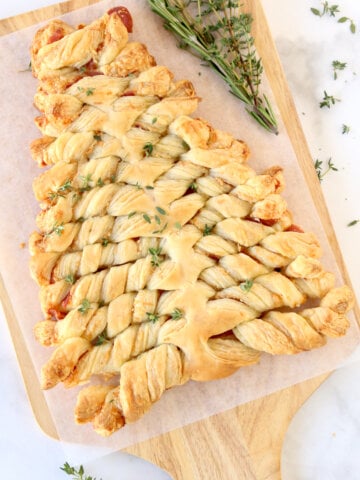 A wood board with a tree shaped puff pastry with fresh herbs next to it.