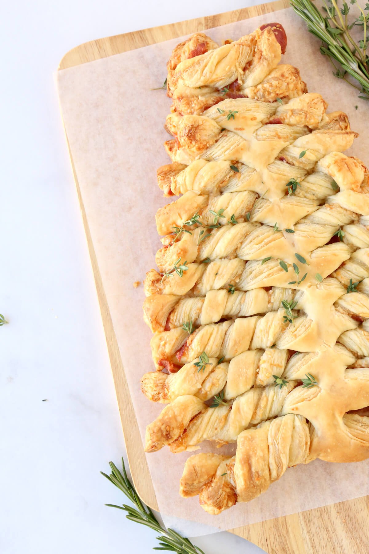 A wood board with a tree shaped puff pastry with fresh herbs next to it. 