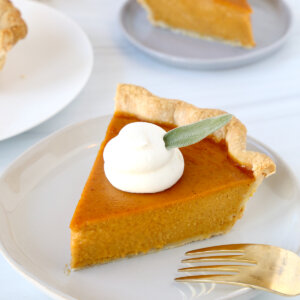 A close up of a pumpkin pie slice with a fork on a plate.
