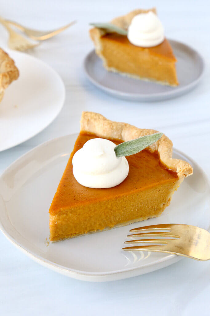 A close up of a pumpkin pie slice with a fork on a plate.