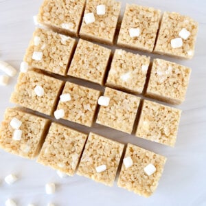 Sixteen square of rice krispie treats with marshmallows sprinkled all over.