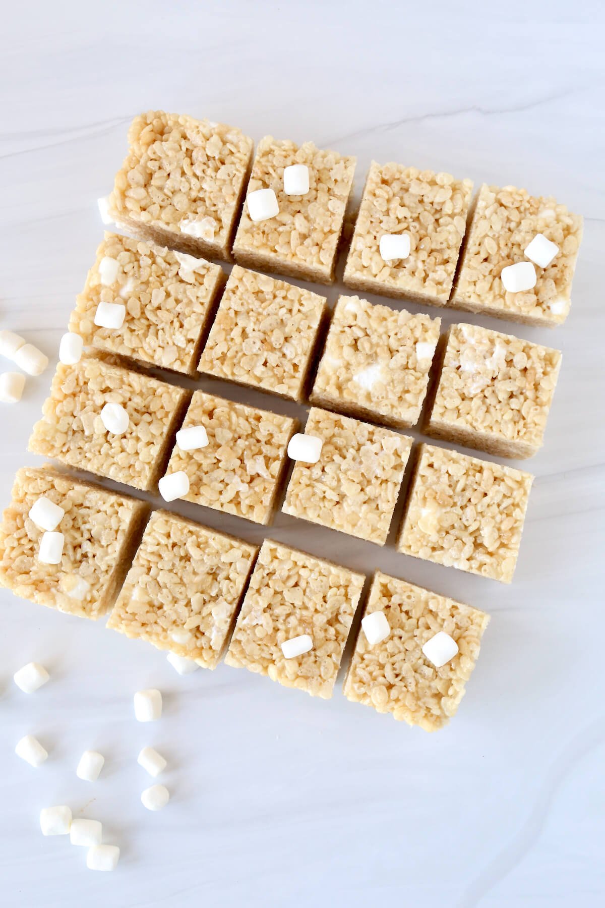 Sixteen square of rice krispie treats with marshmallows sprinkled all over.