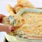 A hand holding a piece of grilled bread with spinach dip on top.