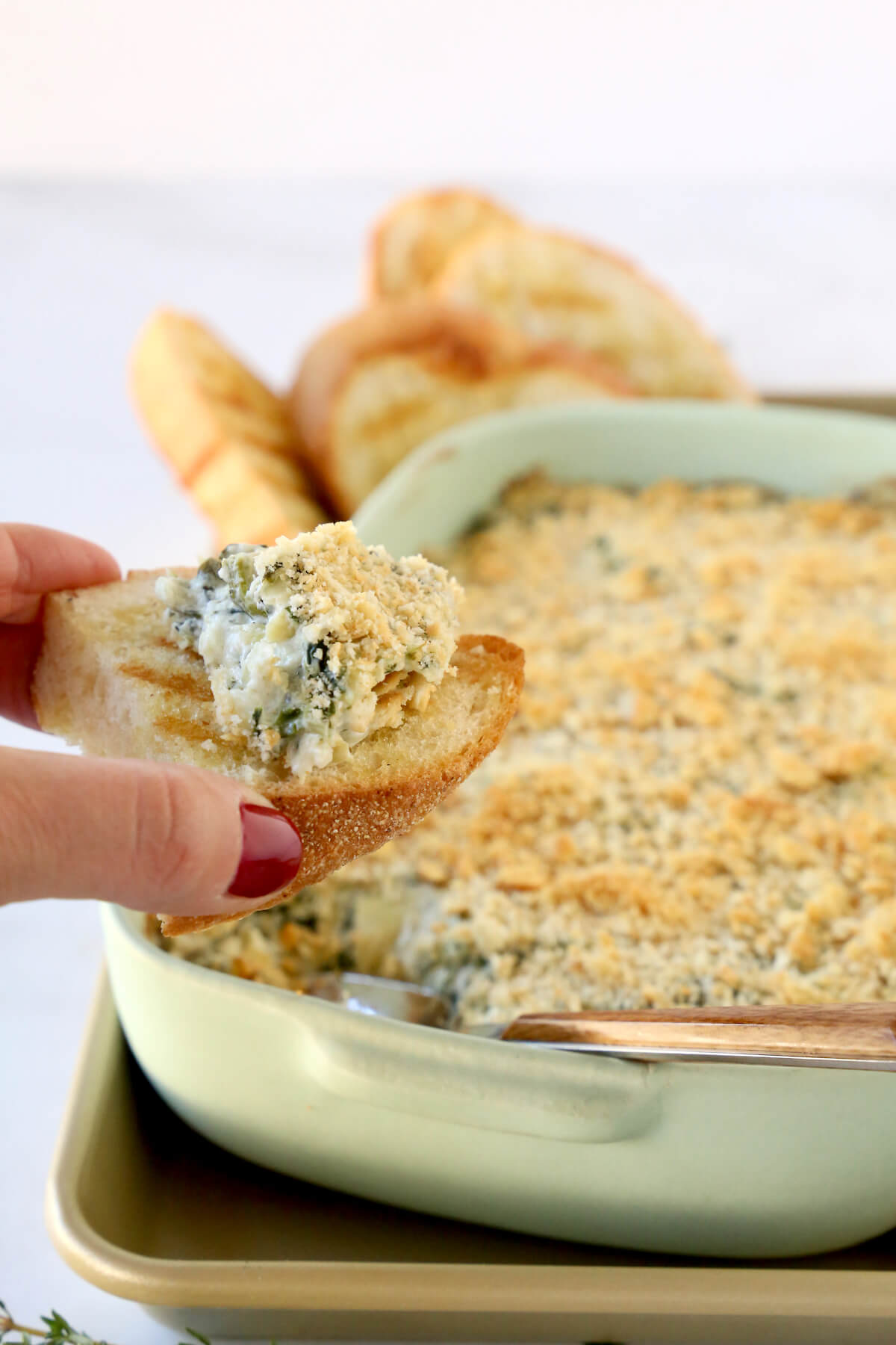 A hand holding a piece of grilled bread with spinach dip on top.
