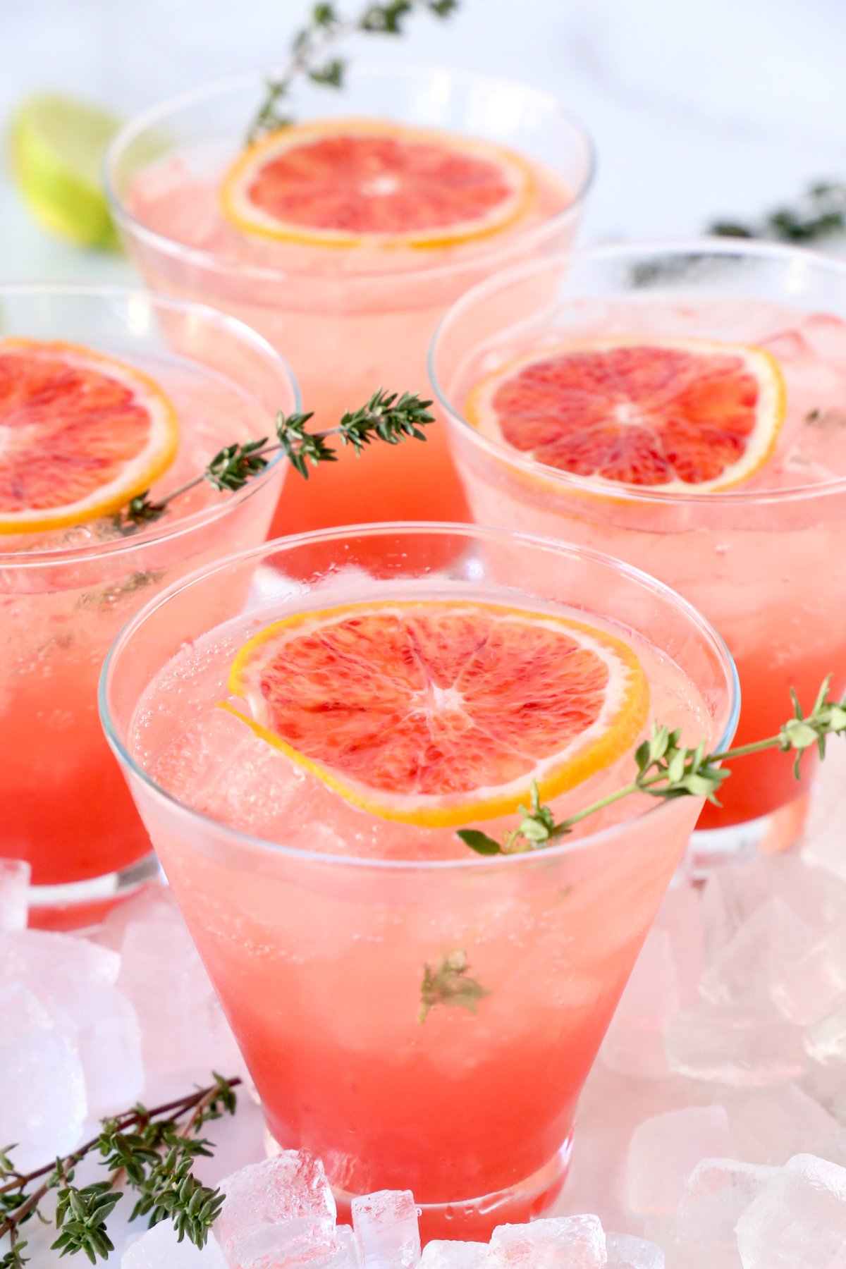 Four glasses or orange liquid with a slice of blood orange and a thyme sprig.