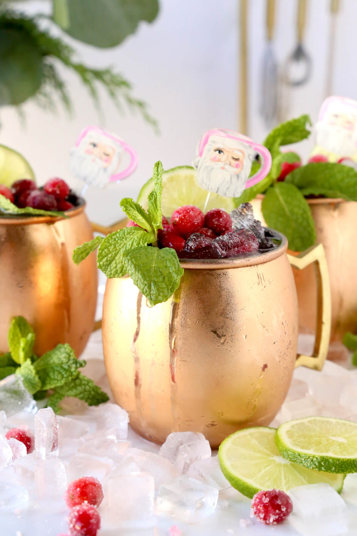 A copper mug filled with ice, cranberries, mint leaves, santa stick and lime.