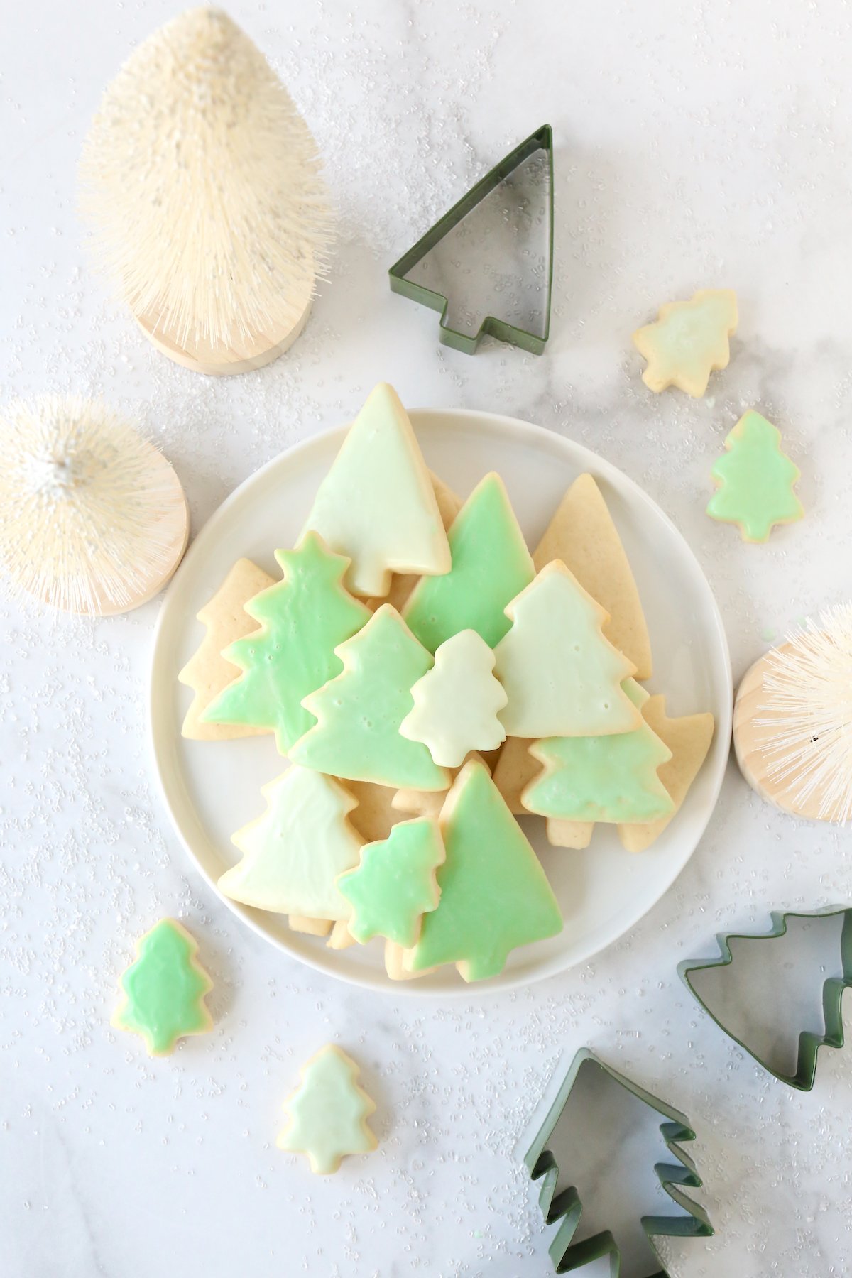A white plate filled with green Christmas tree cookies. 