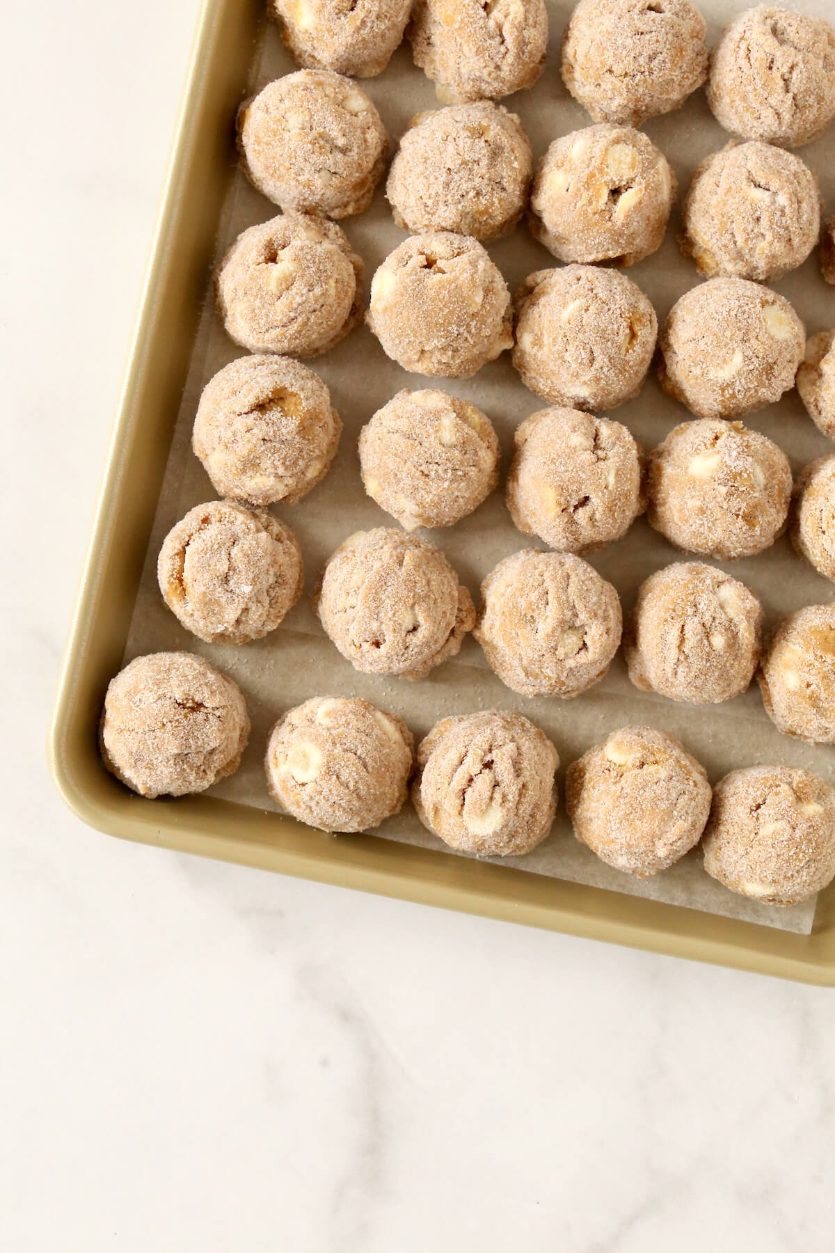 A gold baking pan with scooped cookie dough. 