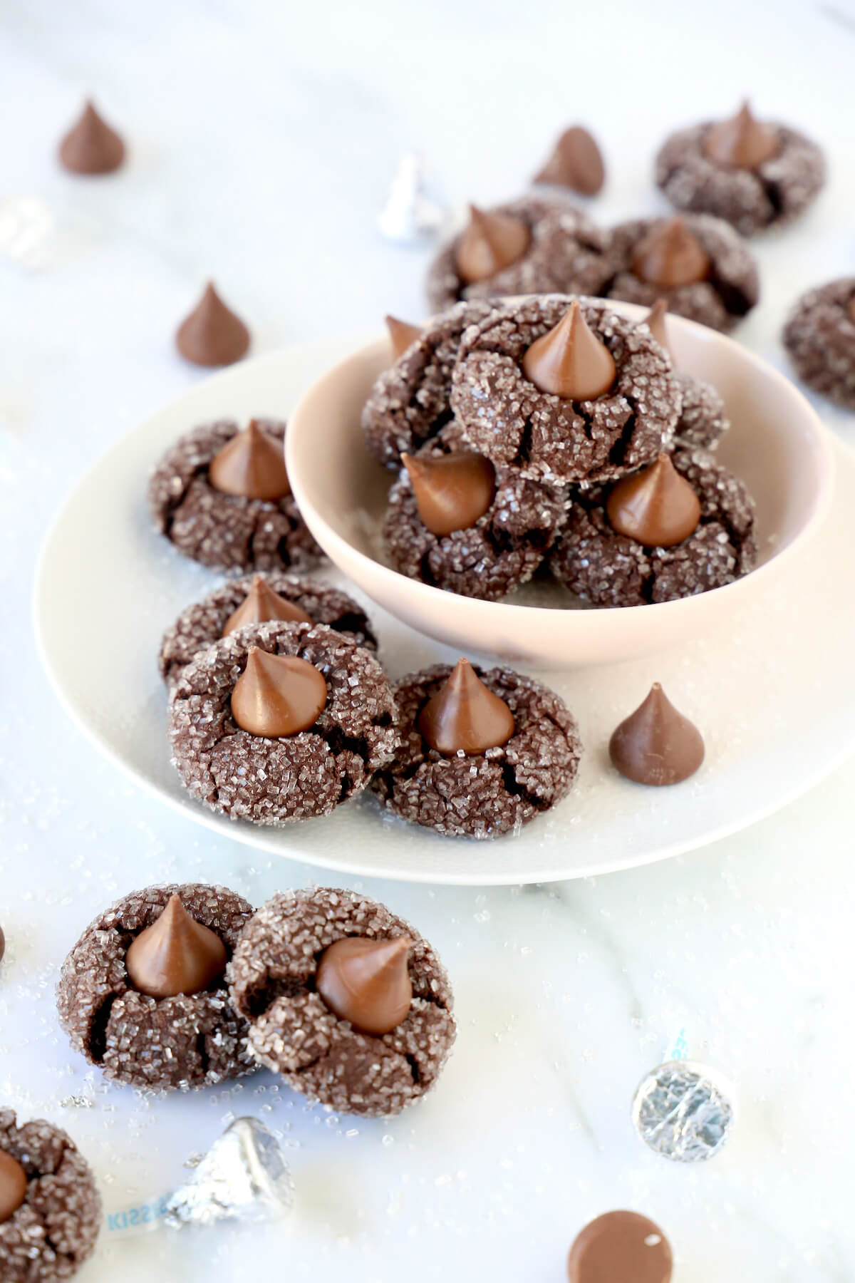 A pink bowls with chocolate cookies with chocolate kisses on top and cookies piled all around the bowl.  