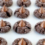 A close up of brown cookies with chocolate kisses on top lined on a baking sheet.