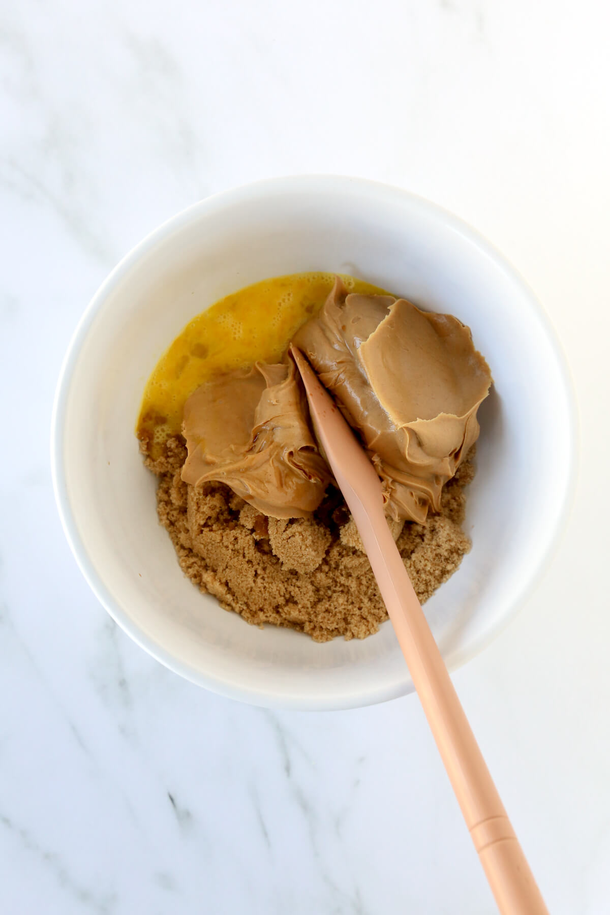 Peanut butter, brown sugar, one egg and vanilla extract in a white bowl.