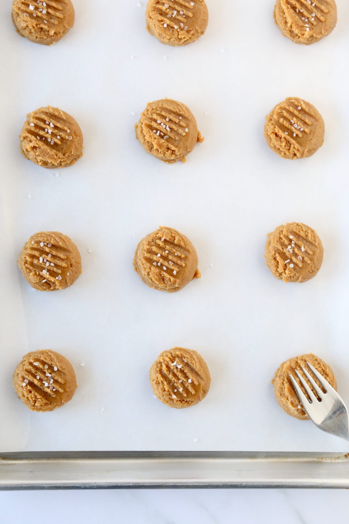Cookie dough on a sheet with with a fork making indentions on the cookies.