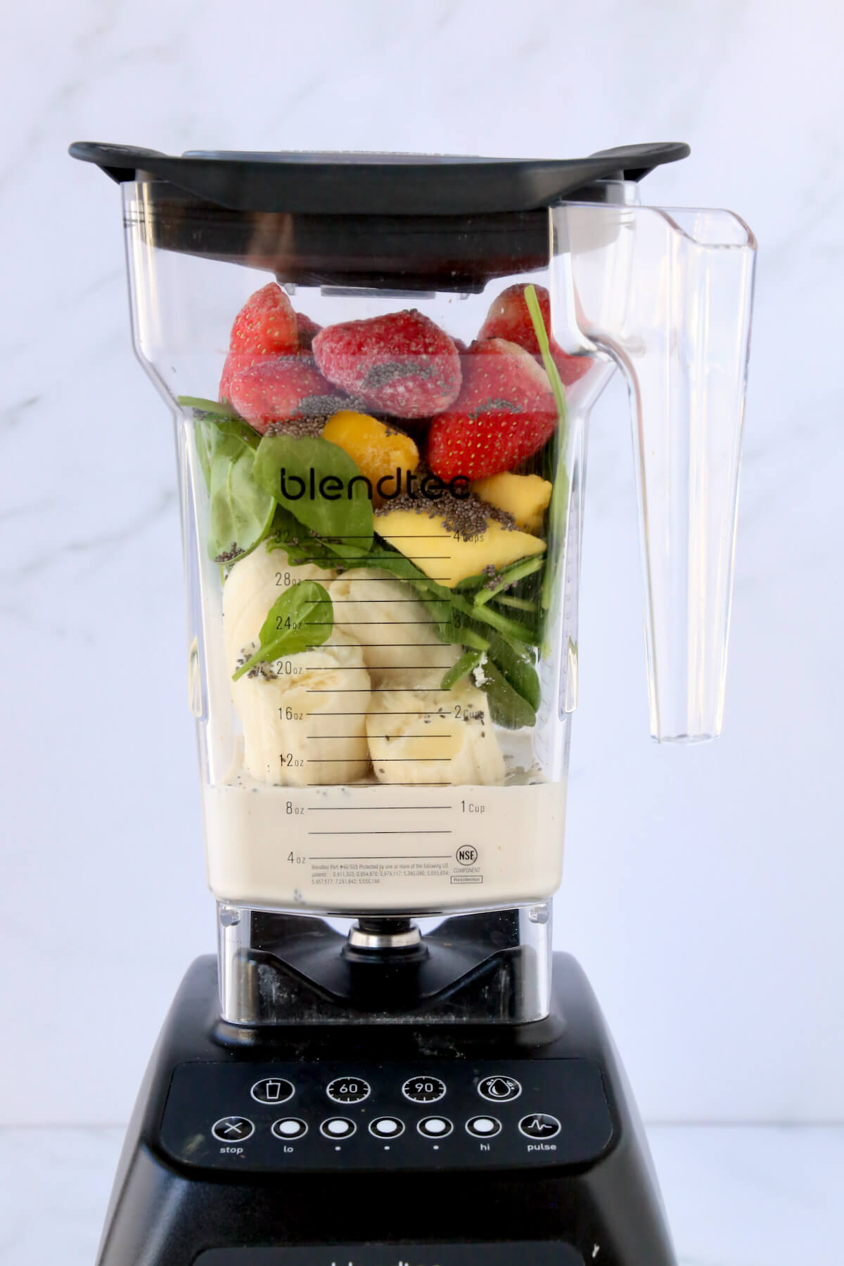 A blender filled with almond milk, bananas, spinach, mango, strawberries.