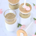 Three cups with tan smoothie with lids and pink flowers.