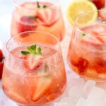 Three clear glasses filled with tequila, rose, lemon juice and sliced strawberries.