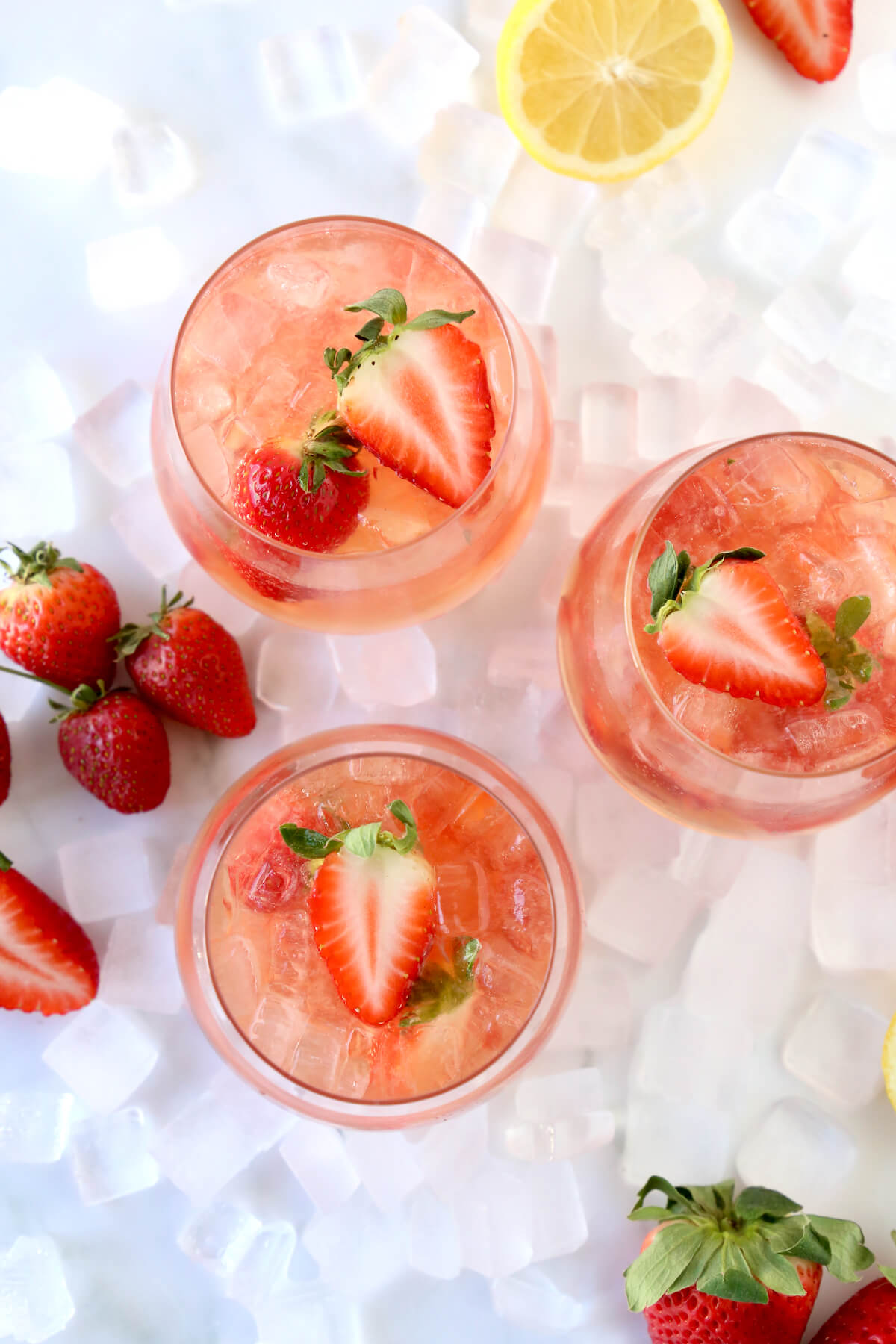 Three clear glasses filled with tequila, rose, lemon juice and sliced strawberries.