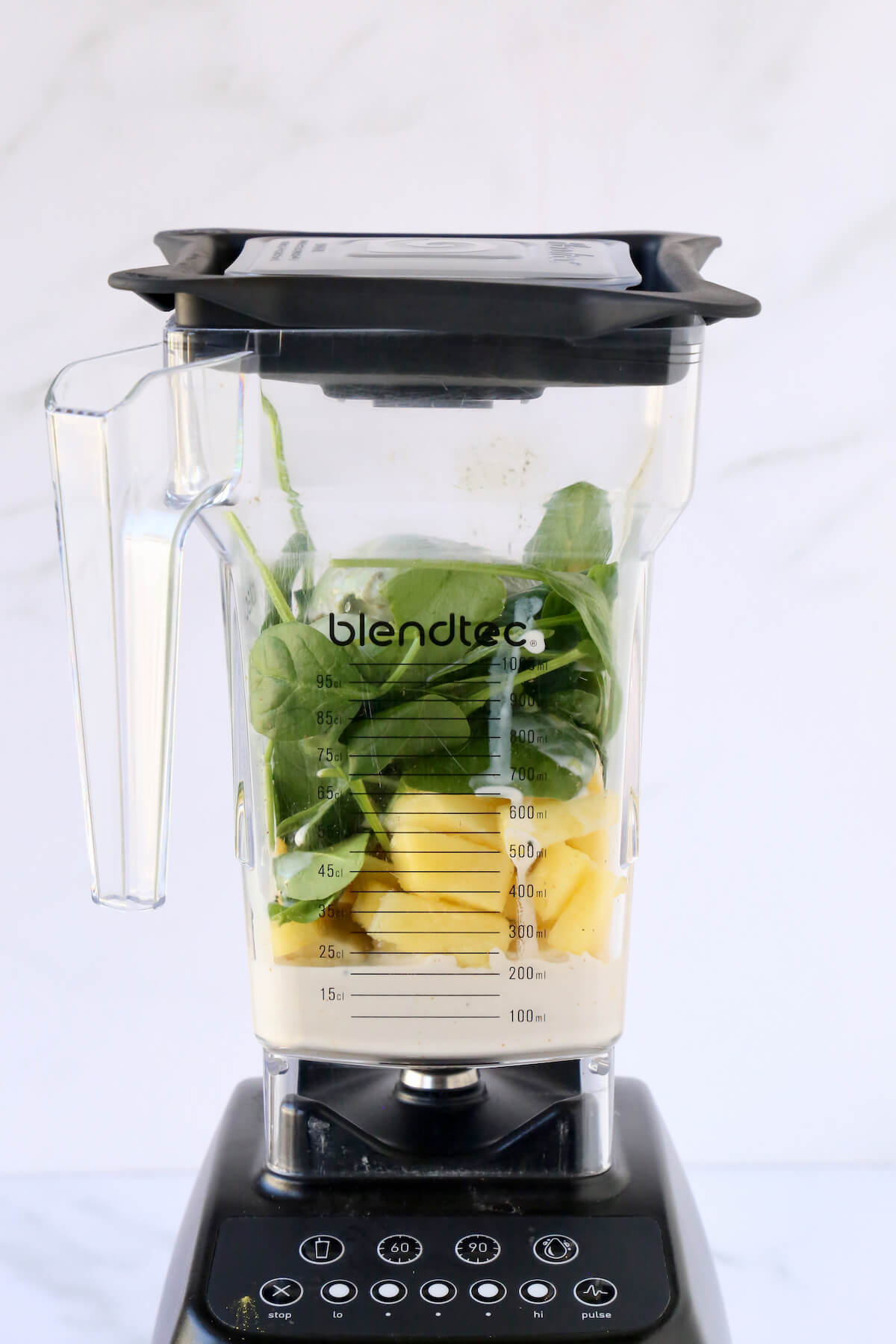 A blender filled with pineapple, spinach, avocado, kiwi and almond milk.