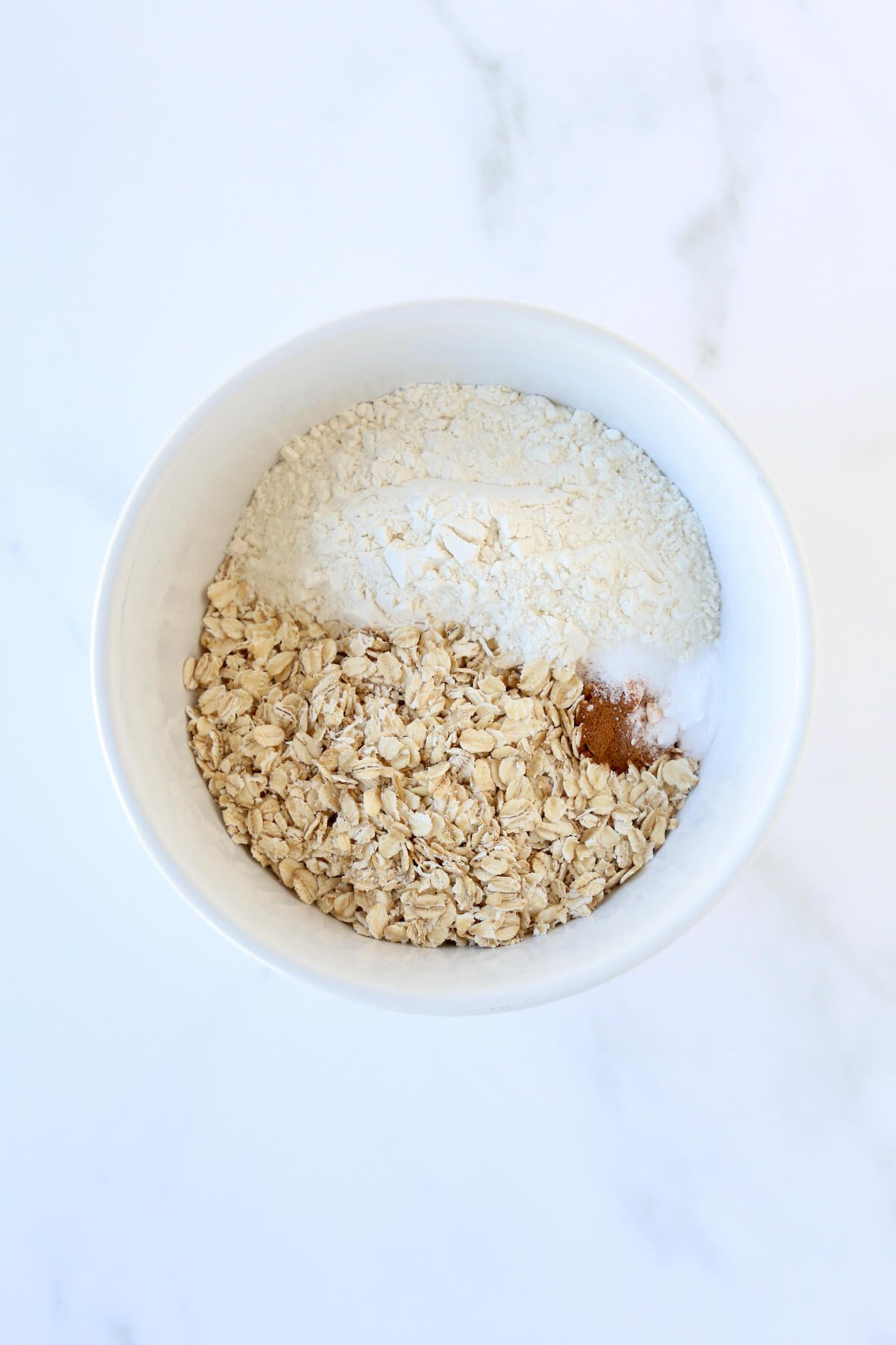 Flour, oatmeal and cinnamon in a white bowl.