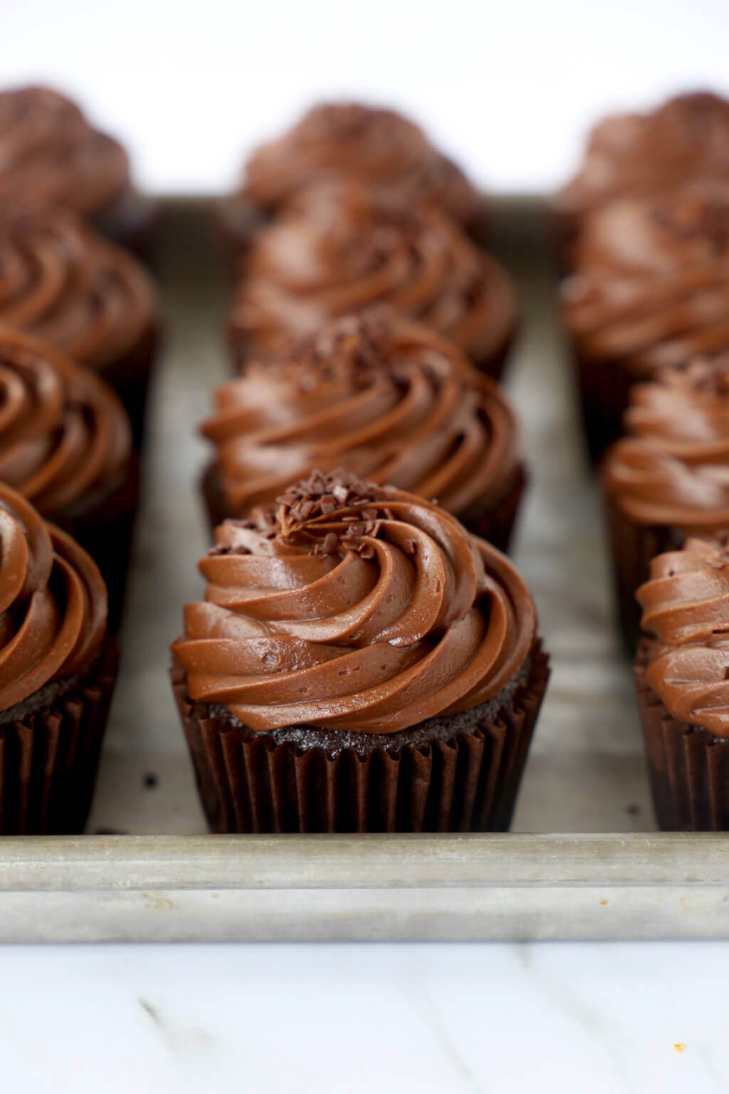A baking sheet lined with brown cupcakes with brown frosting.
