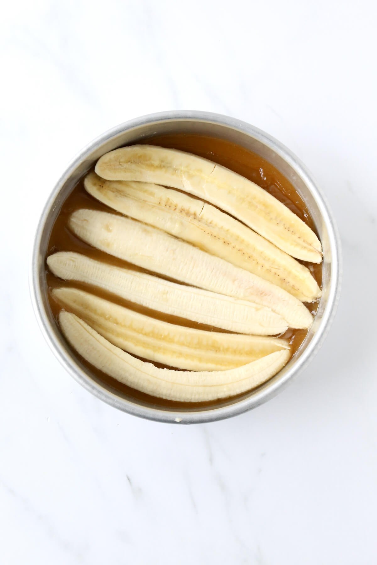 An 8 inch round cake pan filled with caramel sauce and sliced bananas.