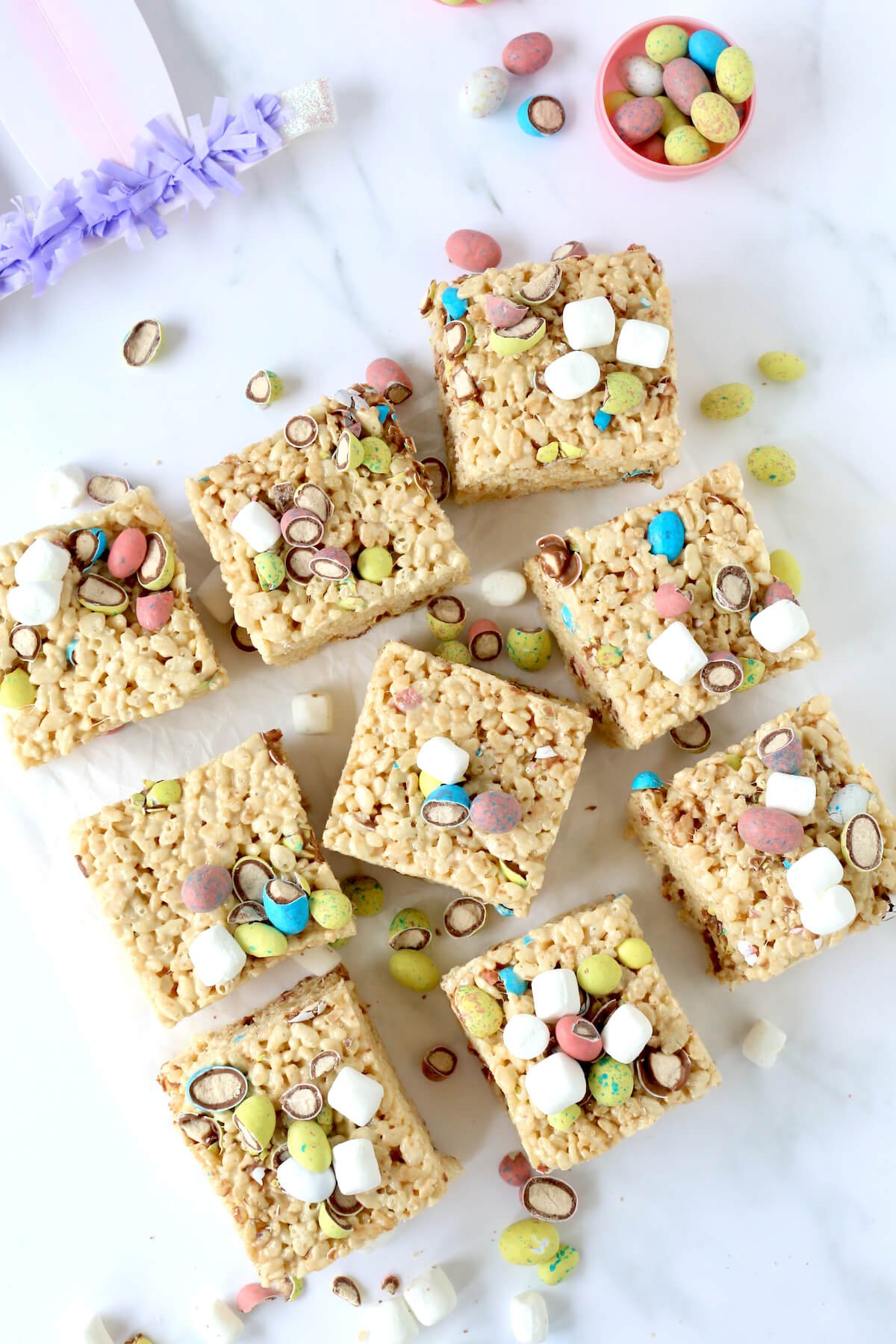 Nine square of rice krispie treats with malted eggs and marshmallows on top.  