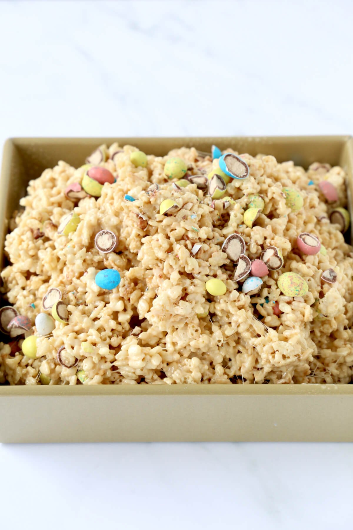 A gold square cake pan filled with the rice Krispie treat mixture. 