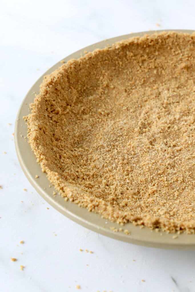 A gold pie plate filled with crush graham crumbs.