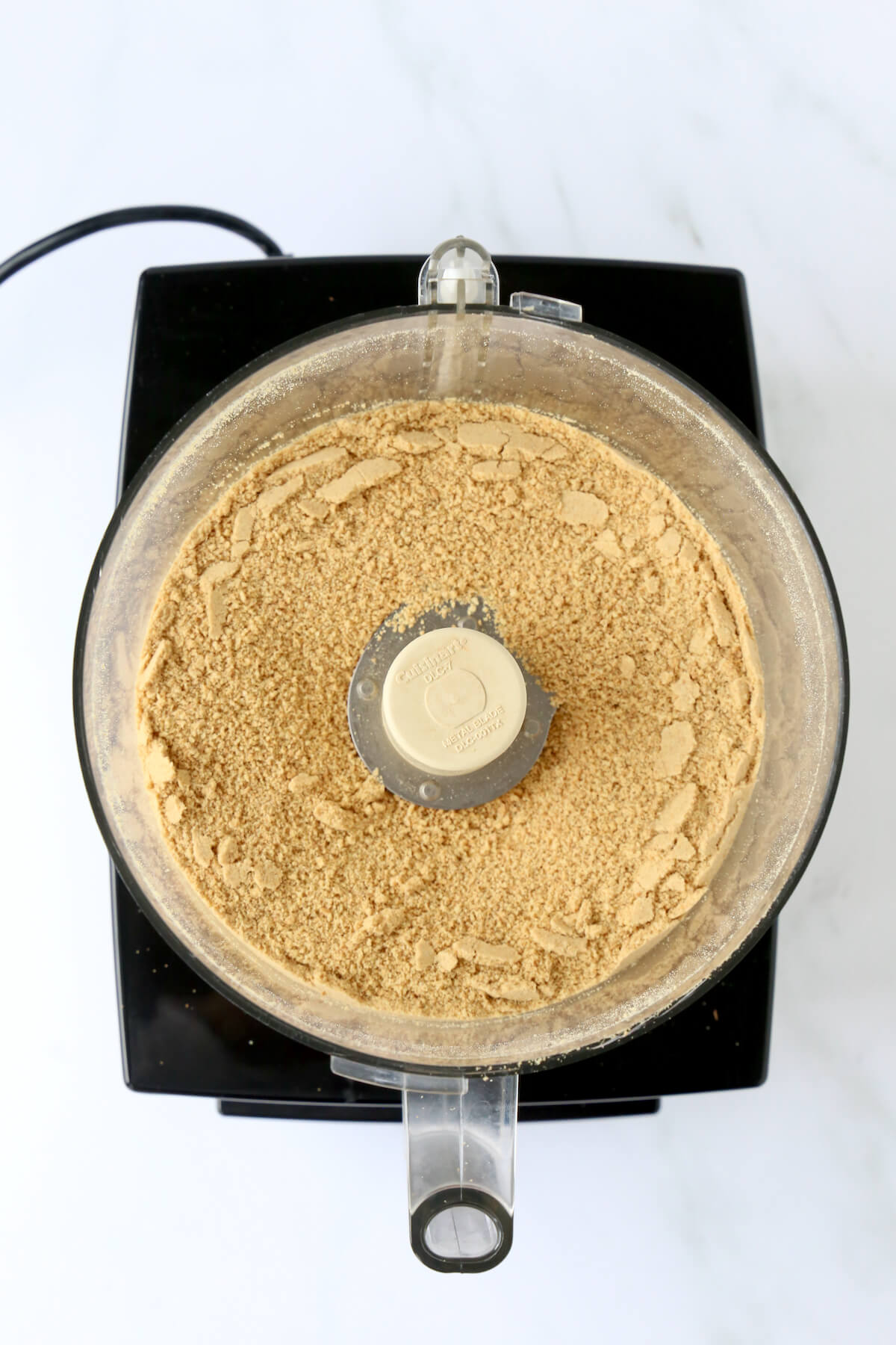A food processor with graham cracker crumbs inside.