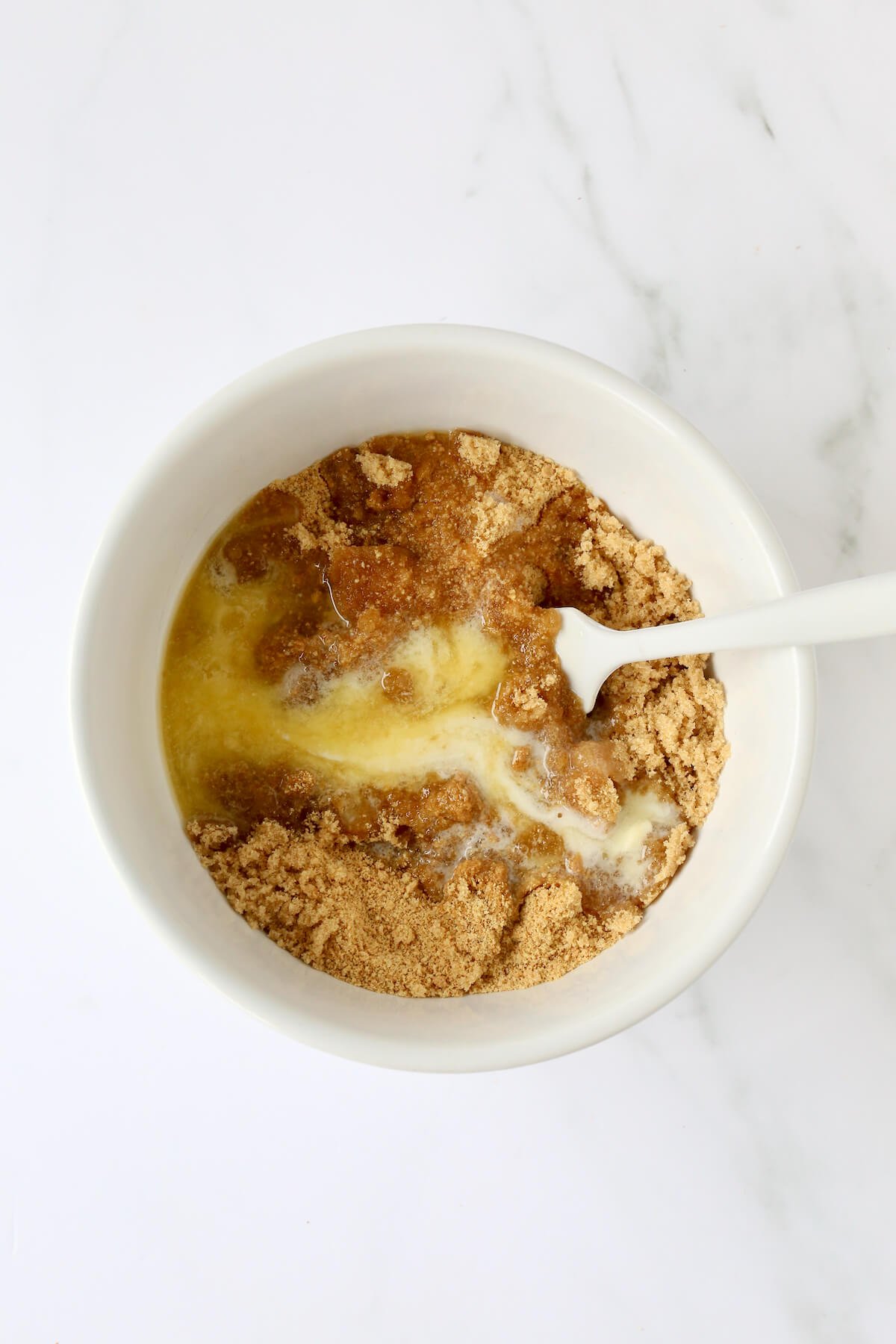 A white bowl filled with graham cracker crumbs, butter and brown sugar.