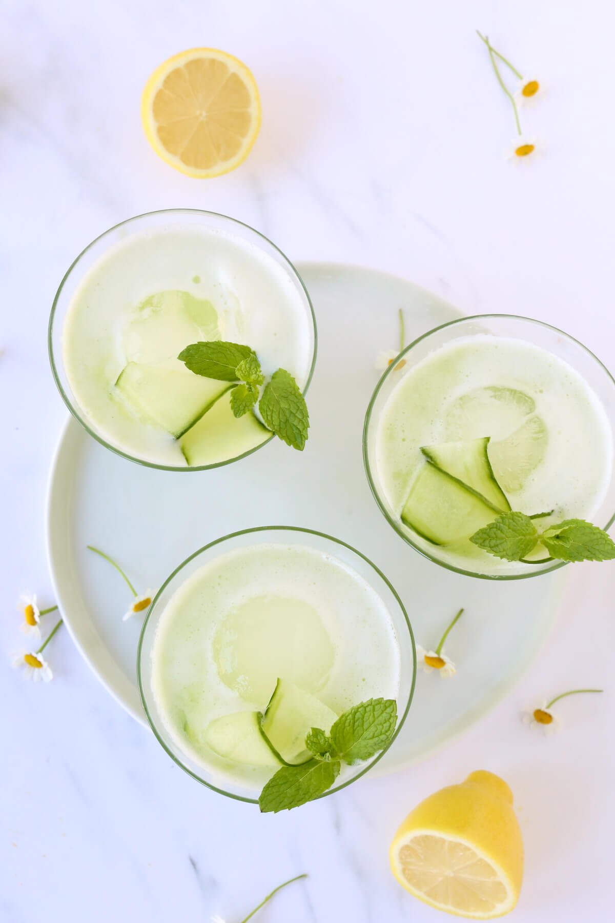 Three glasses filled with a lemon cucumber cocktail topped with fresh mint leaves.