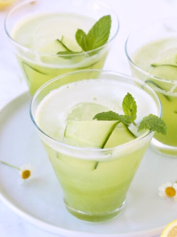 Three glasses filled with green liquid, cucumber and fresh mint.