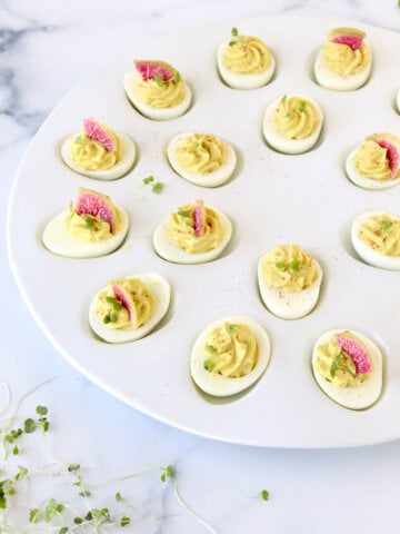 A platter of eggs filled with avocado cream topped with watermelon radishes and micro greens.