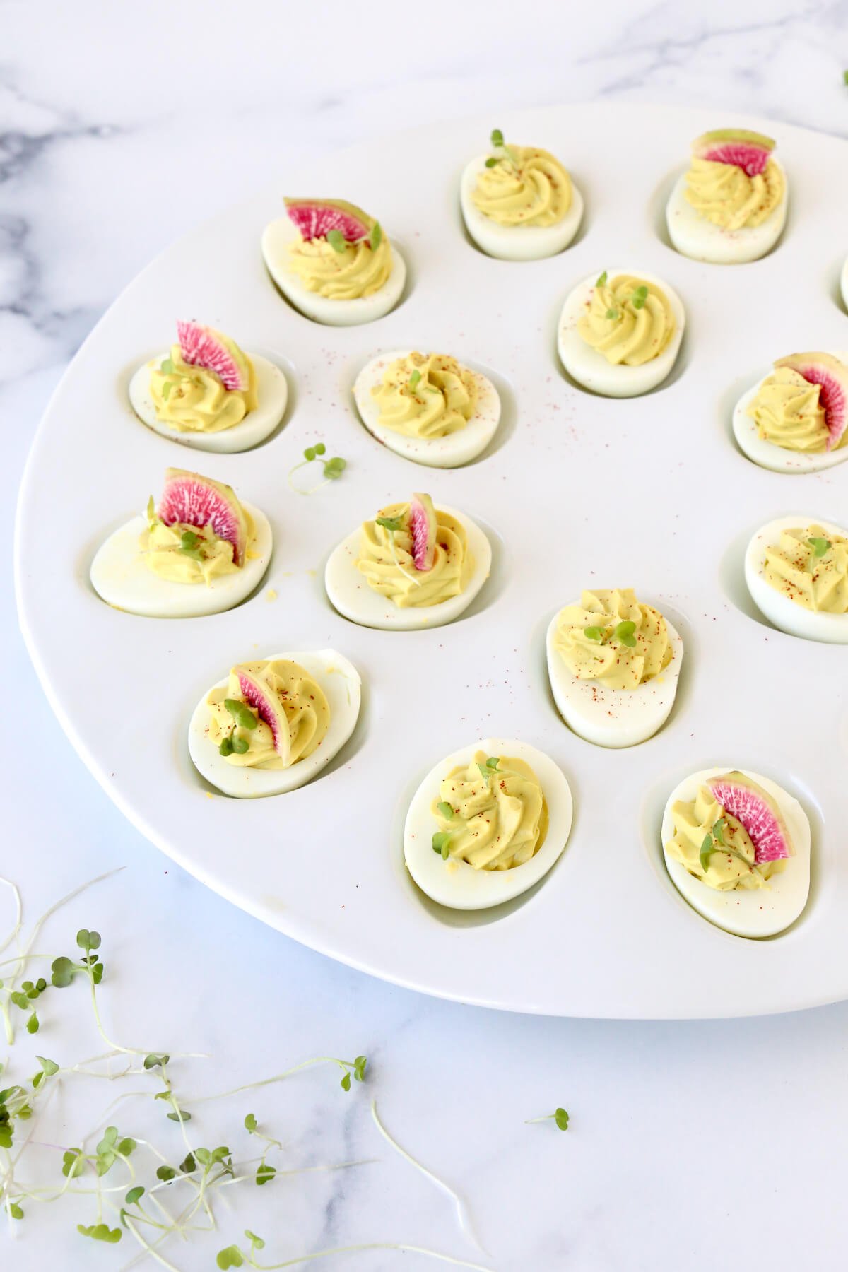 A platter of eggs filled with avocado cream topped with watermelon radishes and micro greens.  