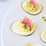 An egg filled with avocado cream and topped with a watermelon radish slice.