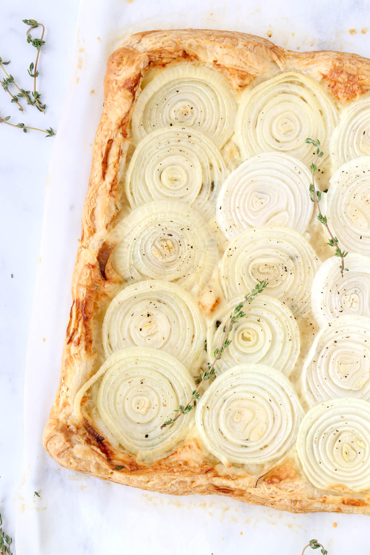 A puff pastry crust with sliced onions on top with fresh thyme leaves