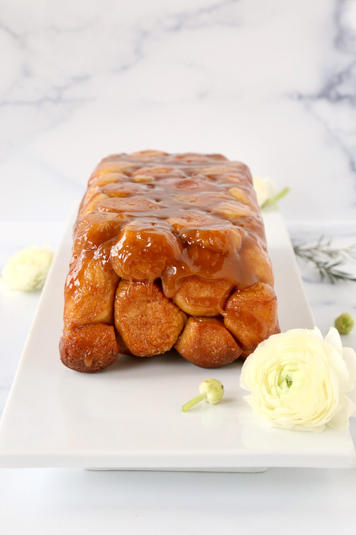 A white platter with a loaf of sweet cinnamon bread on top next to white flowers.  