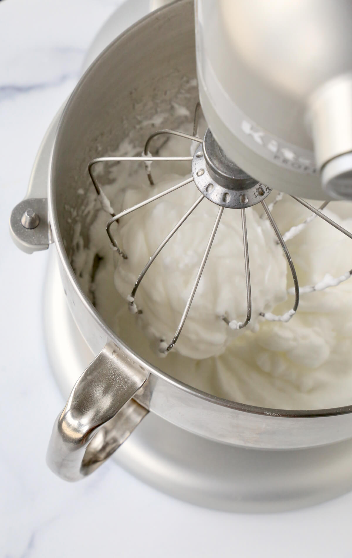 A mixing bowl with whisk attachment and meringue in the bowl.