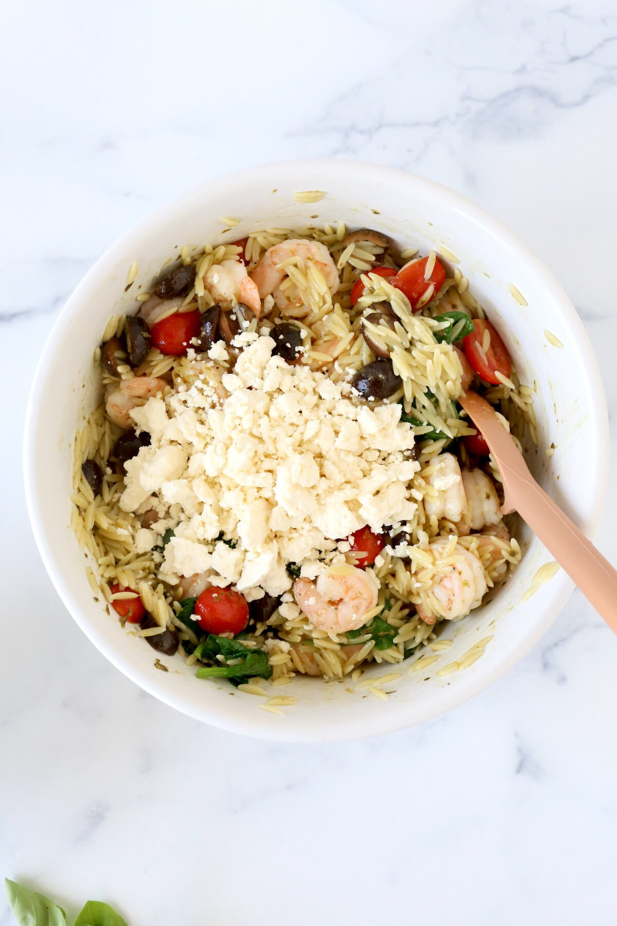A white bowl filled with orzo, shrimp, tomatoes, olives and topped with feta cheese.  