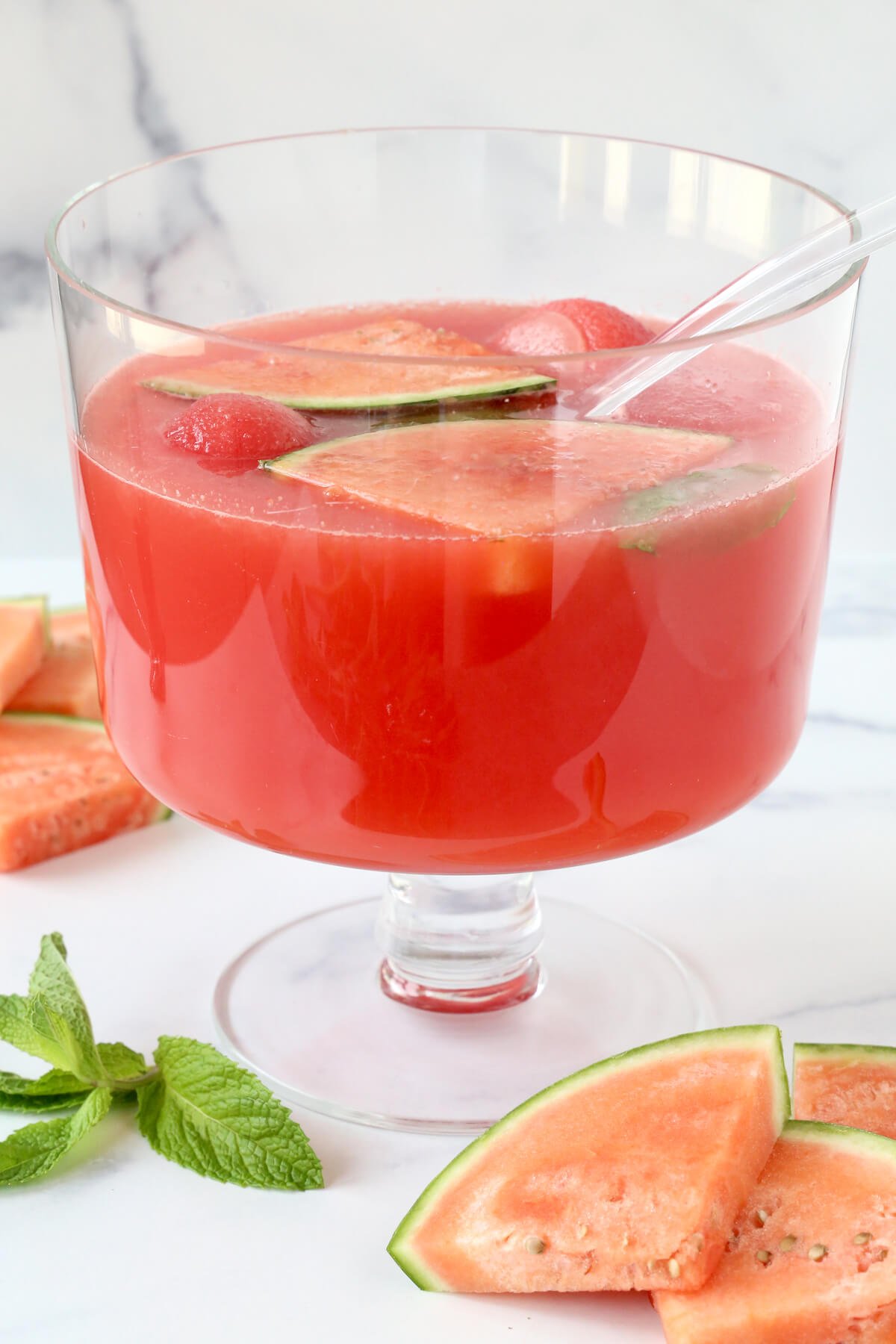 A punch bowl filled with a red liquid, sliced watermelons and watermelon ice cubes 