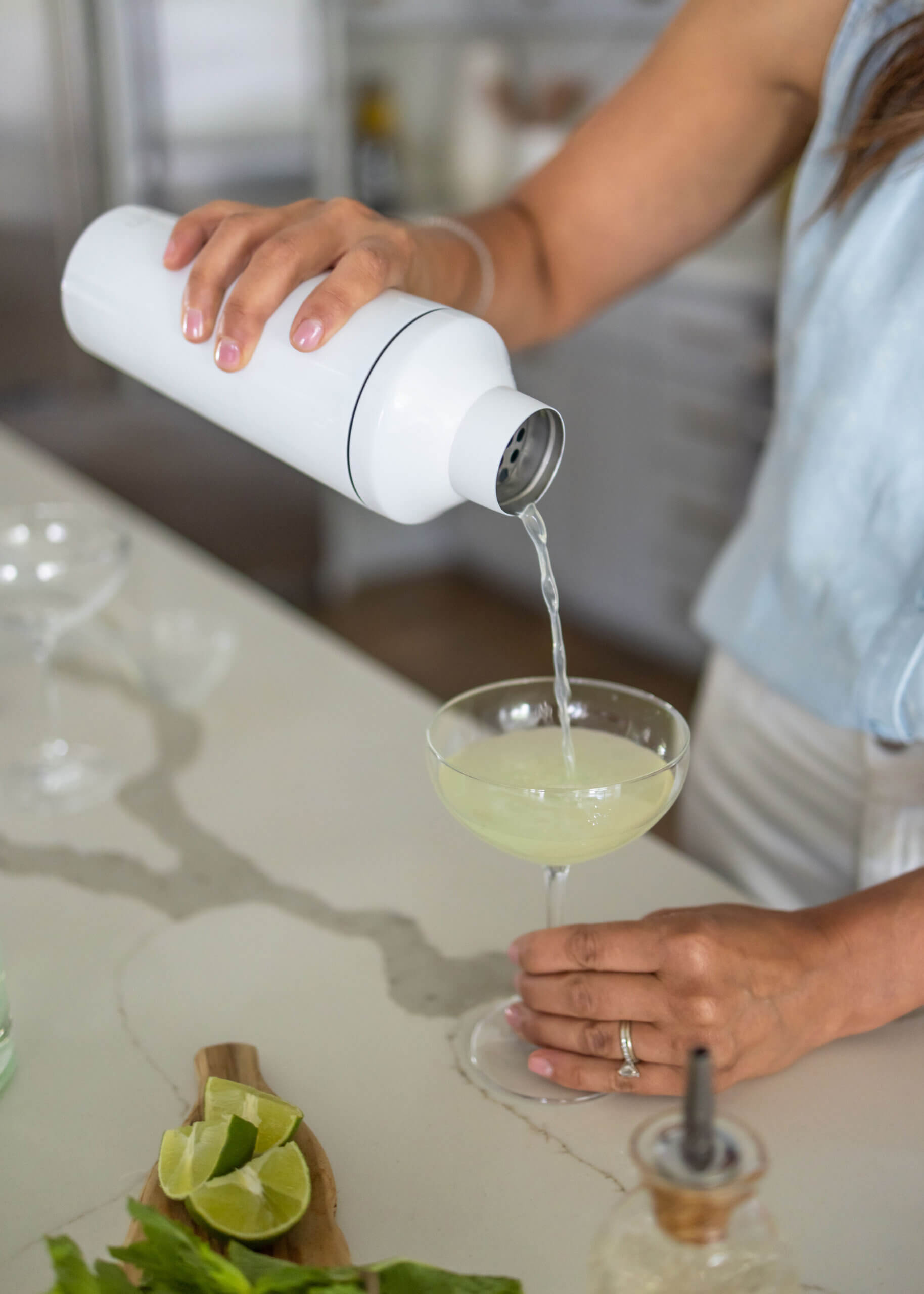 A person pouring a drink from a shaker to a glass.  