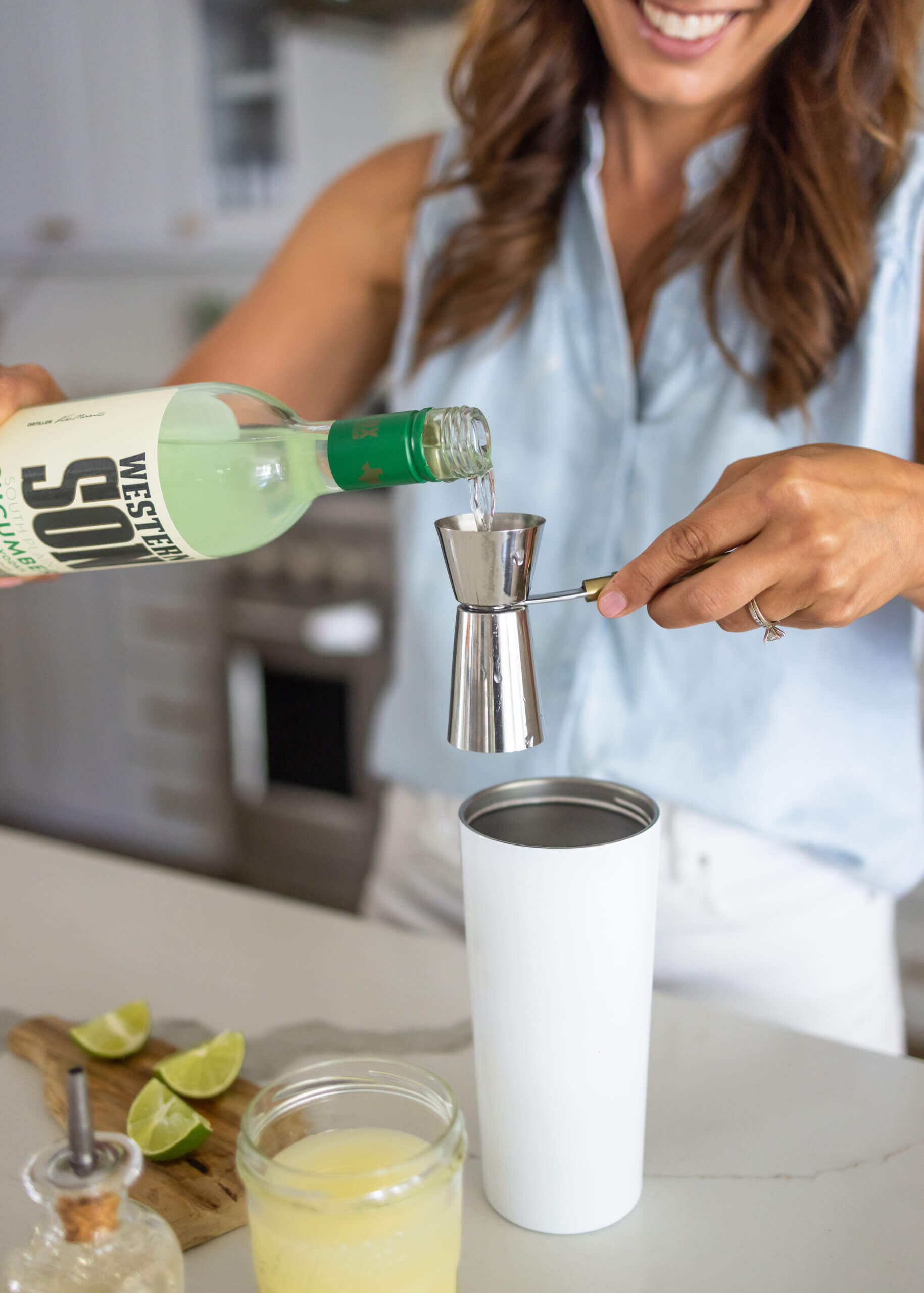 A person pouring cucumber vodka into a measuring cup.