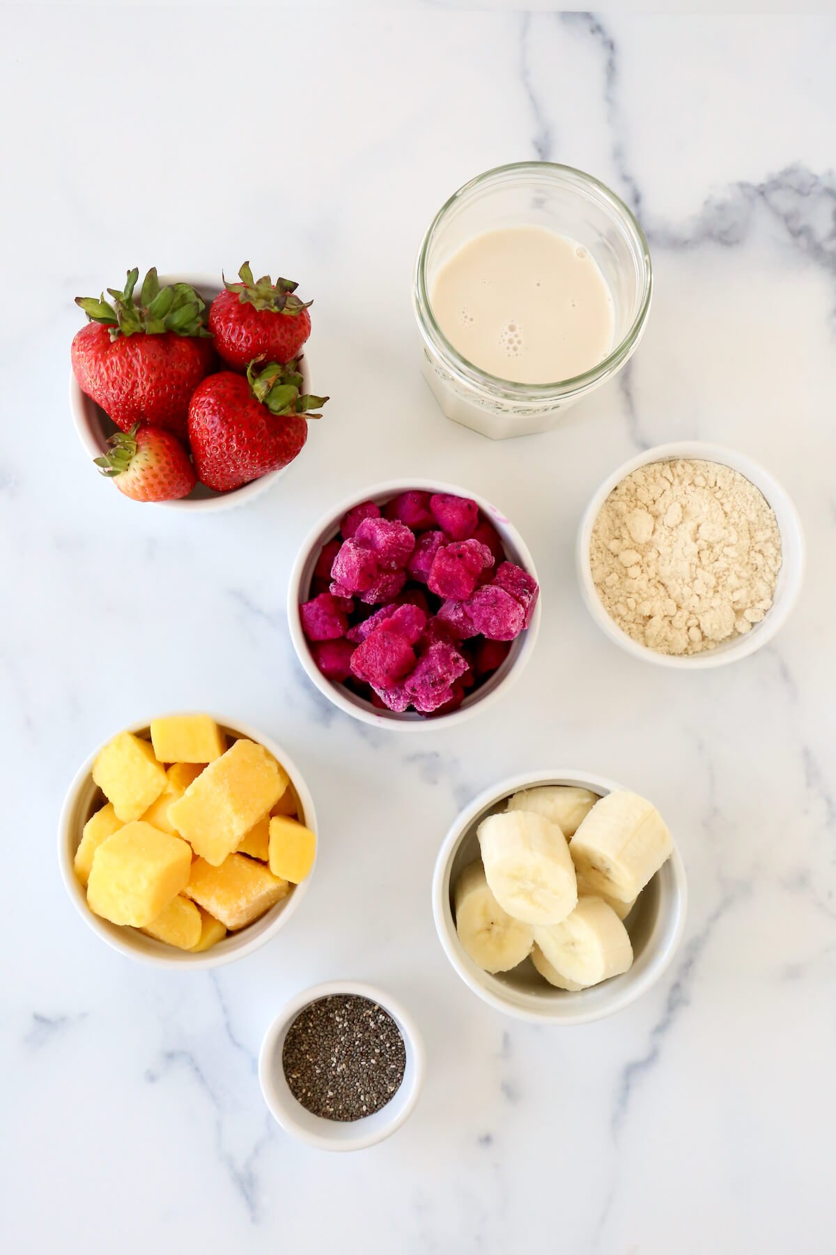 A bowl of strawberries, dragon fruit, frozen mango, bananas, chia seeds and protein powder.  
