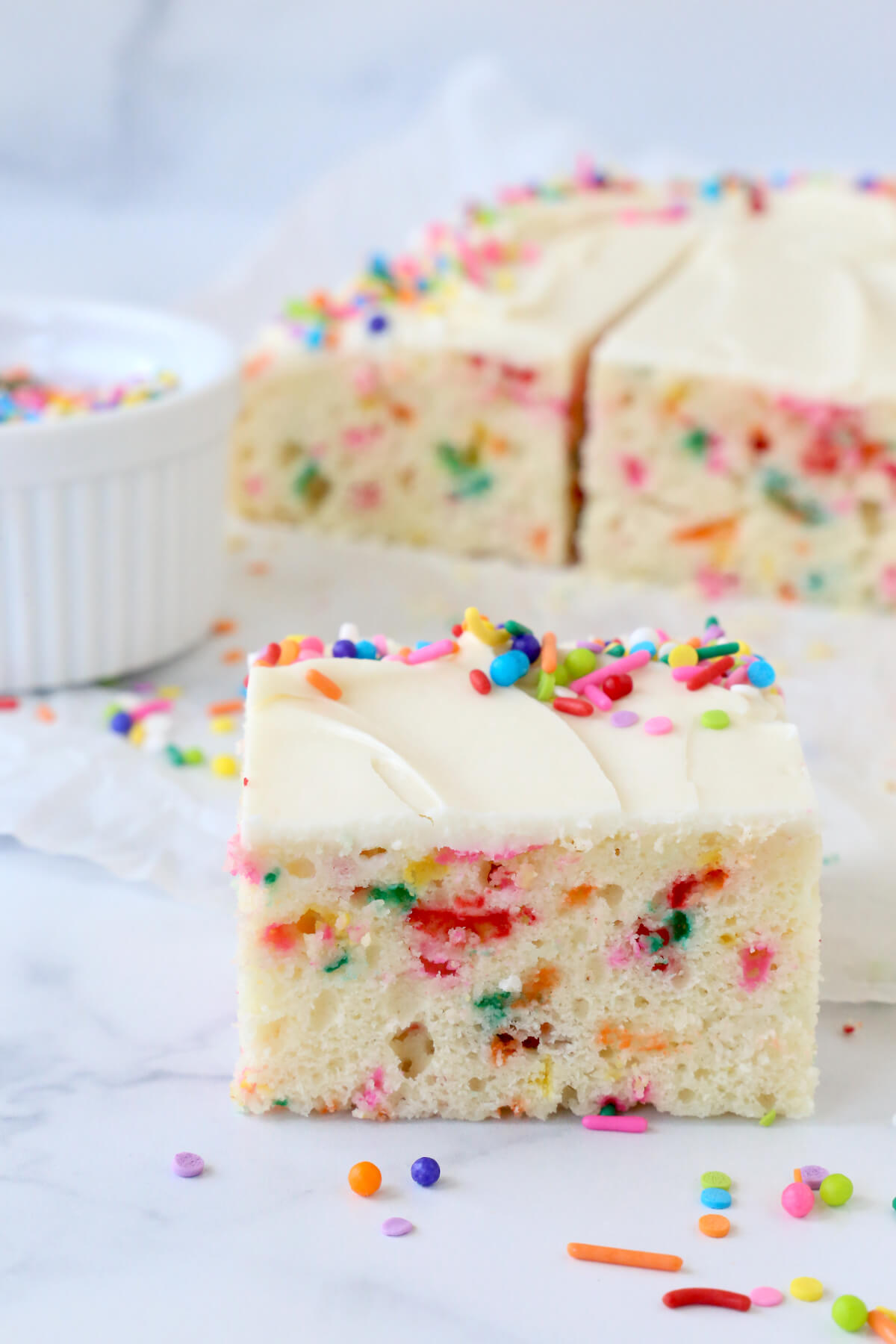 A slice of white cake with rainbow sprinkles.