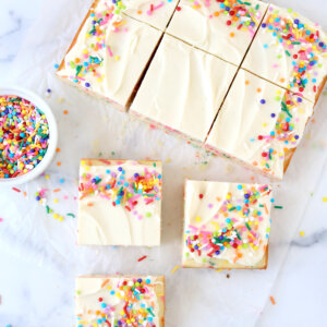 A square cake cut into nine pieces with rainbow sprinkles.